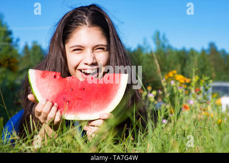 Happy girl eats watermelon outdoors in summer park, healthy food Stock Photo