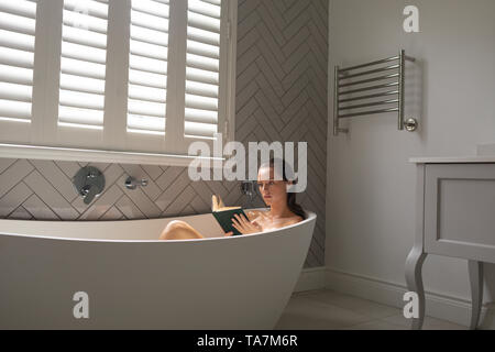 Beautiful woman reading a book in the bathtub Stock Photo