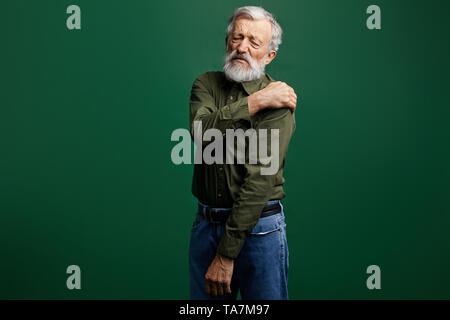 sick old man has pain in neck, senior man has shoulder dislocation. weak man suffering from strong pain. close up photo. isolated green background Stock Photo
