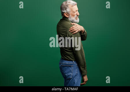 old man massaging his shoulder to reduce pain. close up side view photo. studio shot.isolated green background. Stock Photo