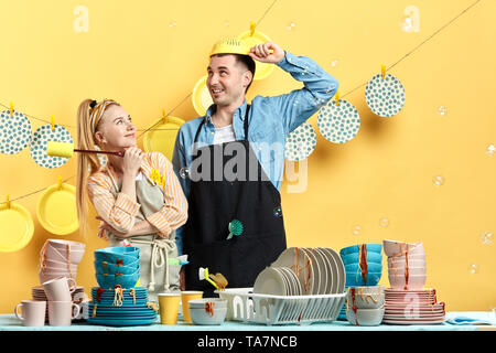 crazy positive man putting on the colander while his pensive smiling wife holding a washing tool and watching him, close up photo. studio shot. Stock Photo