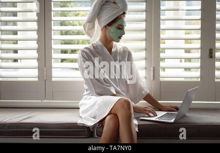 Woman in bathrobe using a laptop near the window Stock Photo