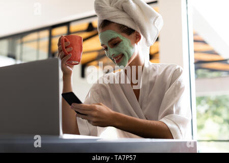 Woman in bathrobe checking her phone while having coffee Stock Photo