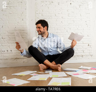Happy successful entrepreneur man surrounded by papers calculating budget and bills at new empty studio office home. In Small business owner, Finances Stock Photo