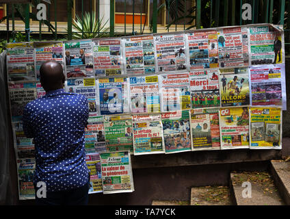 African man reading newspapers displayed on a market stall, Région des Lagunes, Abidjan, Ivory Coast Stock Photo