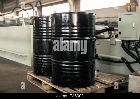Black metal barrel of combustive-lubricating chemicals is on a wooden pallet at the production site. Stock Photo