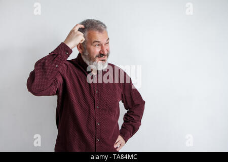 Half-length portrait of a serious gray-haired bearded man in a burgundy shirt on a white background. Stock Photo