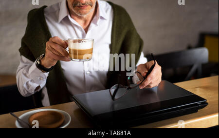 Senior man using laptop and having a cup of coffee in the bar Stock Photo