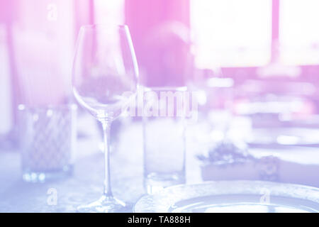 Wine glass at celebration and dining table setting with flowers decorations on light pink blue gradient background. Stock Photo