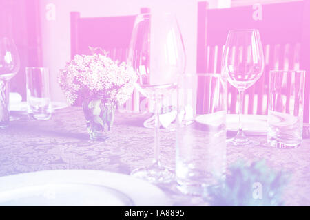 Wine glass at celebration and dining table setting with flowers decorations on light pink blue gradient background. Stock Photo