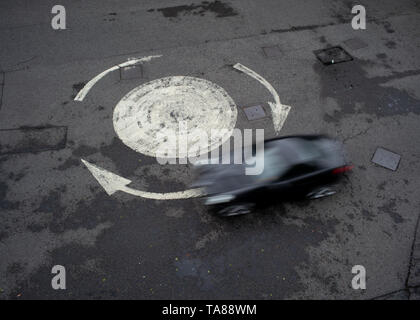 Aerial view of a painted arrowed roundabout with a single car going around. Could be used as an analogy or concept as being lost or going in circles. Stock Photo