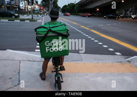 A Grab Food cycle rider on the streets of Singapore delivering food waiting at a crossing of a busy road as a rain storm moves in for a dramatic image. Stock Photo