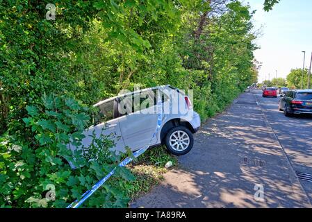 A white saloon car face down in a ditch after crashing off a main road, Shepperton Surrey England UK Stock Photo