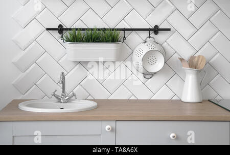 Wooden kitchen sink counter with plant pot and different utensils Stock Photo