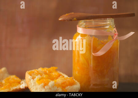 A jar of orange marmalade with a spoon and some rolls where the marmalade has been Stock Photo