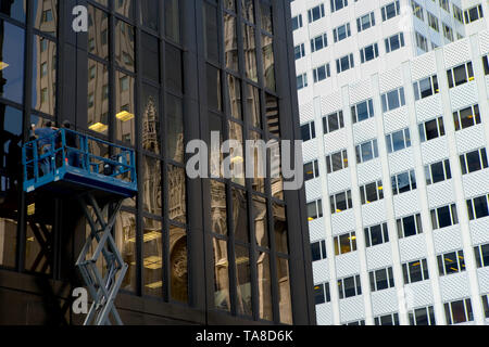 Two Workers on Lift Repairing Glass Building Façade with Reflection of Saint Patrick's Cathedral, New York City, New York, USA Stock Photo