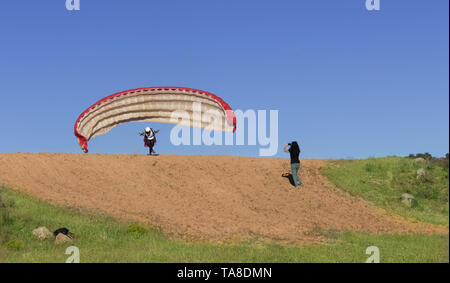 Female paraglider pilot taking off and woman filming with her mobile, with a blue sky in the background Stock Photo