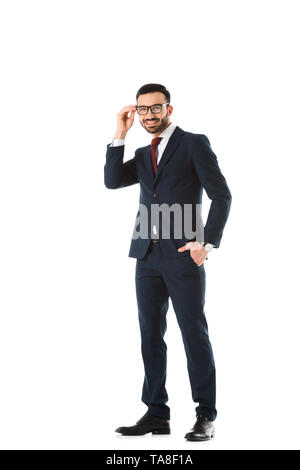 smiling businessman standing with hand in pocket, touching glasses and looking at camera isolated on white Stock Photo