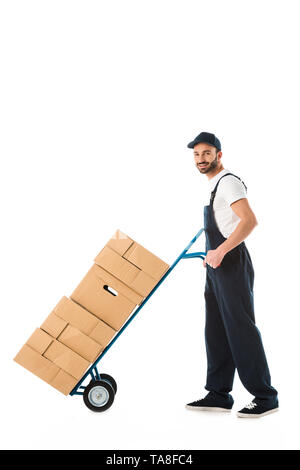 smiling delivery man transporting hand truck loaded with carton boxes isolated on white Stock Photo