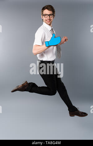 smiling businessman in glasses with paper cut thumb up jumping on grey background Stock Photo