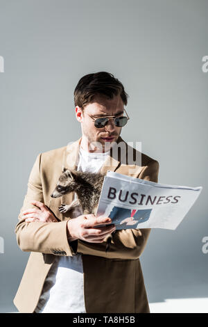 attentive man in sunglasses, with funny raccoon on shoulder, reading business newspaper Stock Photo