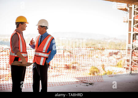 Two executives in safety gear talk on construction site. Stock Photo