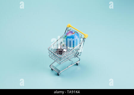 a disco ball and a planet earth in a supermarket shopping cart turquoiseon a turquoise background. Minimal still life color photography Stock Photo