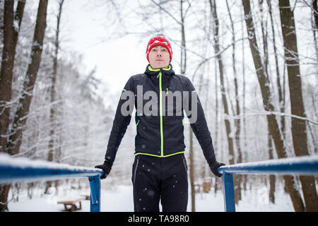 Photo of sports man on horizontal bar in winter at woods Stock Photo