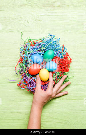 Photo of multicolored easter eggs and hand on green wooden background Stock Photo
