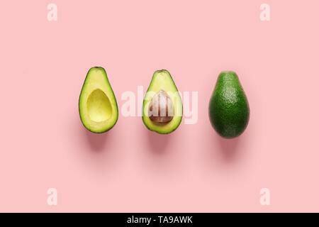 Whole avocado fruit and two halves in a row isolated on pink background Stock Photo