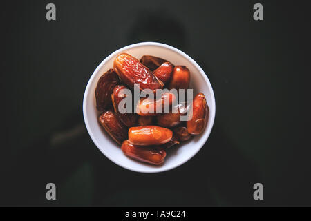 Dried whole dates in the white bowl holding in hand taken from the top on a black background. Stock Photo
