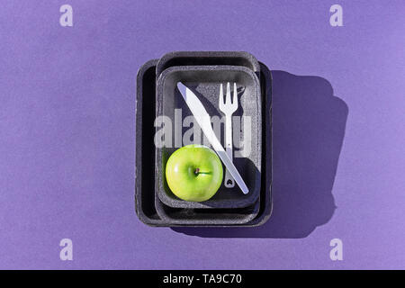 Top view of an empty plastic tray with green apple and disposable tableware on purple, flat lay. Concept of reducing the use of plastic Stock Photo