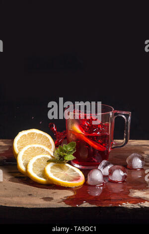 Summer iced drink - hibiscus cold tea with ice, lemon and mint.  Big splash with drops of hibiscus cold tea from the glass of beverage with fallen lem Stock Photo
