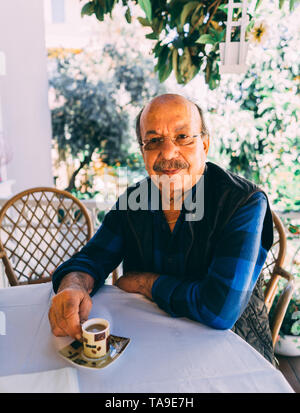 Elderly man sitting at the table and drinks turkish coffee. Old man enjoys his cup of coffee outside on spring day. Stock Photo