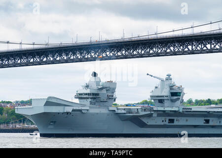North Queensferry, Scotland, UK. 23rd May, 2019. Aircraft carrier HMS Queen Elizabeth sails from Rosyth in the River Forth after a visit to her home port for a refit. She returns to sea for Westlant 19 deployment and designed to focus on the operations of her F-35 fighter aircraft. Pictured; Carrier passes underneath the Forth Road Bridge Bridge at low tide. Credit: Iain Masterton/Alamy Live News Stock Photo