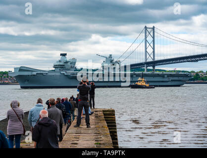 North Queensferry, Scotland, UK. 23rd May, 2019. Aircraft carrier HMS Queen Elizabeth sails from Rosyth in the River Forth after a visit to her home port for a refit. She returns to sea for Westlant 19 deployment and designed to focus on the operations of her F-35 fighter aircraft. Pictured; People gathered at North Queensferry pier to watch the carrier depart the River Forth. Credit: Iain Masterton/Alamy Live News Stock Photo