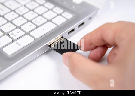 Human hand plugging in an SD media card into the personal laptop computer on white background Stock Photo