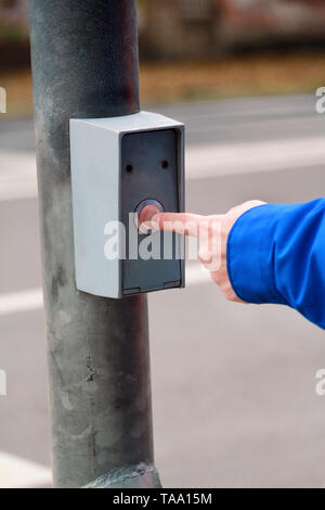 Portrait of male hand pressing button for crossing street on crosswalk and traffic light. Man standing on traffic light and pedestrian crossing. Stock Photo