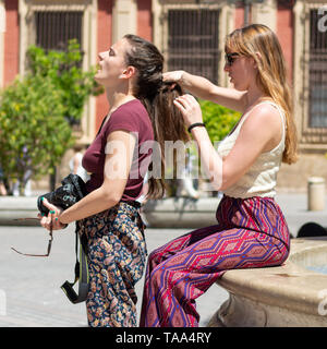 Girl plaiting hair for a friend in a public space on a hot day. Stock Photo