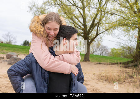 A young couple on the beach wearing them piggyback Stock Photo