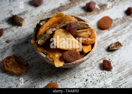 closeup of a rustic earthenware bowl full of assorted dried fruit, such as pear, peach, banana, strawberry, apple or apricot, on a white rustic wooden Stock Photo