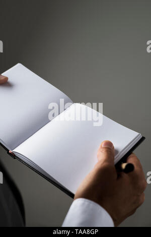 closeup of a young caucasian man, in an elegant suit, with a blank notebook in his hands, on a gray background with some blank space on top Stock Photo