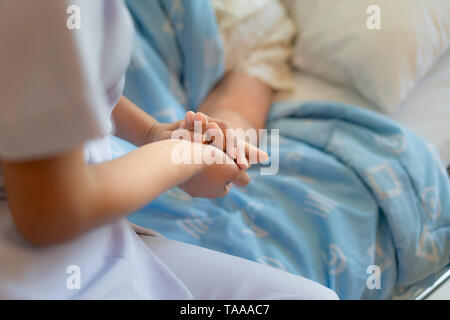 Nurse sitting on a hospital bed next to an older woman helping hands, care for the elderly concept Stock Photo