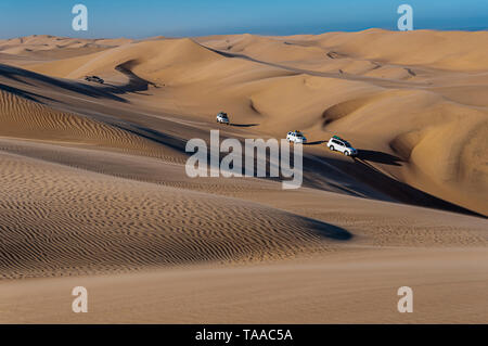 Four-wheel drive vehicles follow in a convoy as they tour through the Namib desert of Namibia. Stock Photo
