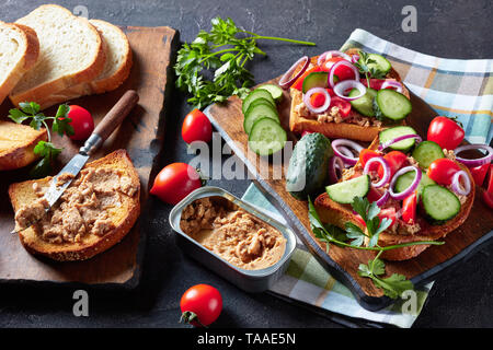 close-up of toasts with Cod Liver pate, topped with sliced cucumber, tomatoes and red onion rings on a cutting board with ingredients on a kitchen tab Stock Photo