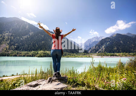 Tourist woman with rising hat and cowboy hat enjoying beautiful view of lake in the mountains in Kazakhstan Stock Photo