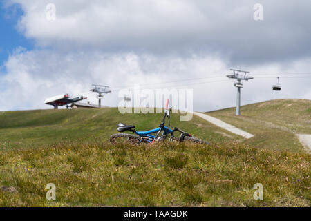 Full suspension downhill mountain bike lying on ground, mountains over Livigno with cableway in backround, sunny summer day, Italy Stock Photo