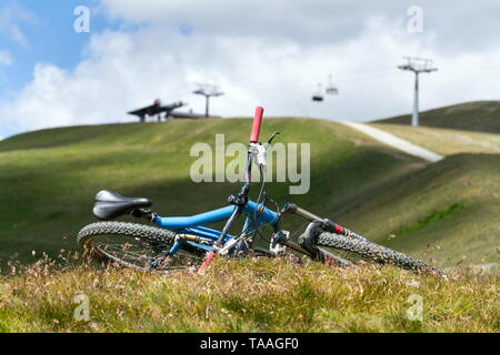 Full suspension downhill mountain bike lying on ground, mountains over Livigno with cableway in backround, sunny summer day, Italy Stock Photo