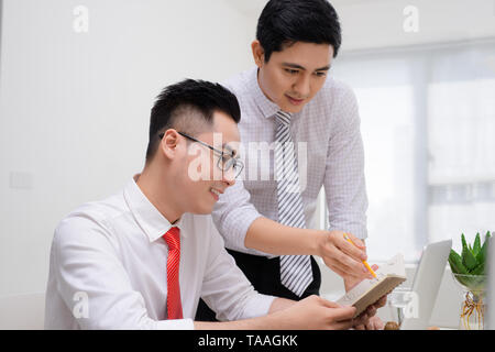 Two businessmen working together with computer at office desk, one of them pointing at screen. Stock Photo
