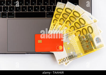 Banknotes of different denominations lie near the laptop, and from the top there is a plastic card Stock Photo